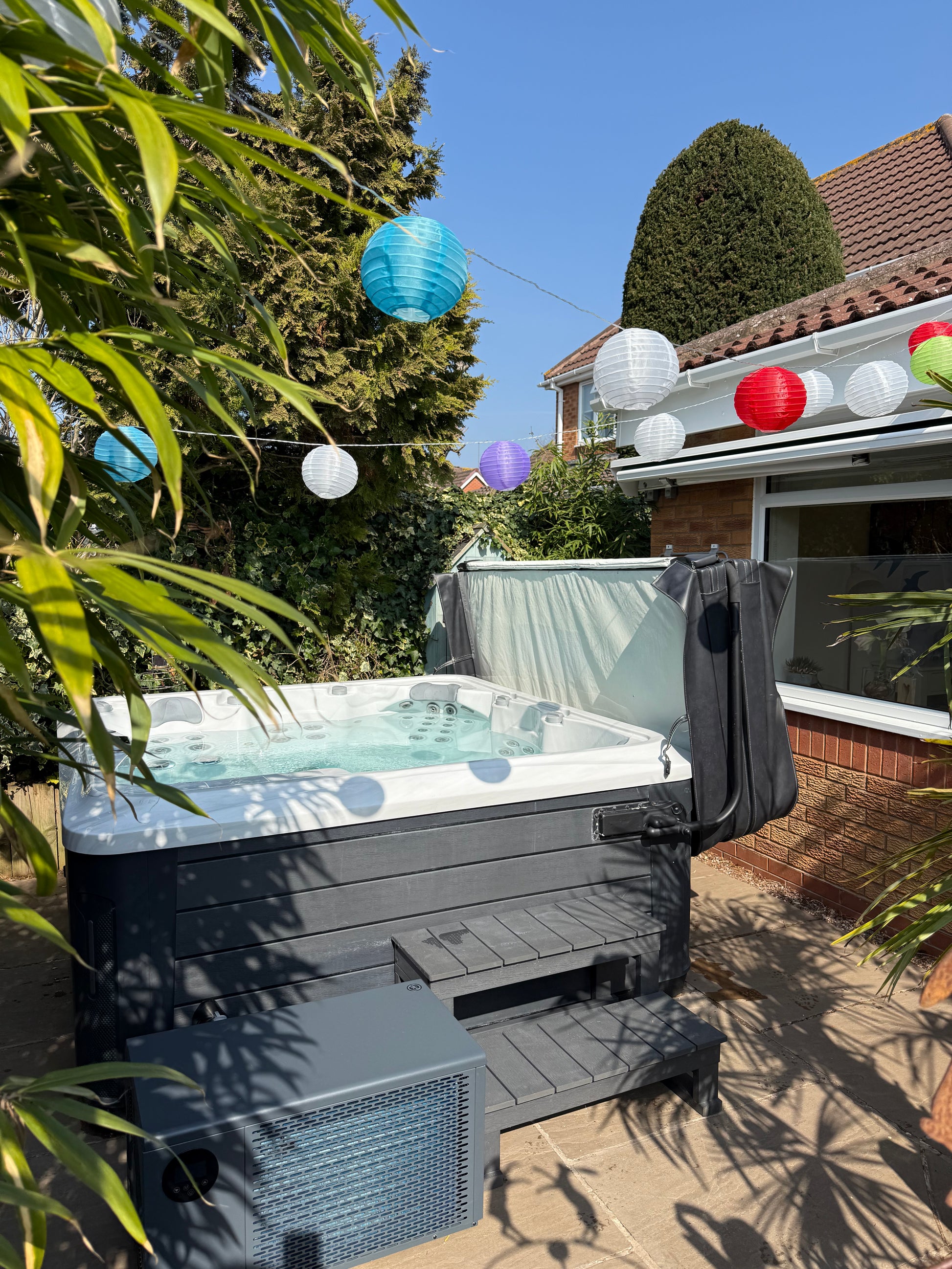Hot tub in a garden with colorful balloons and a house in the background with air source heat pump installed 
